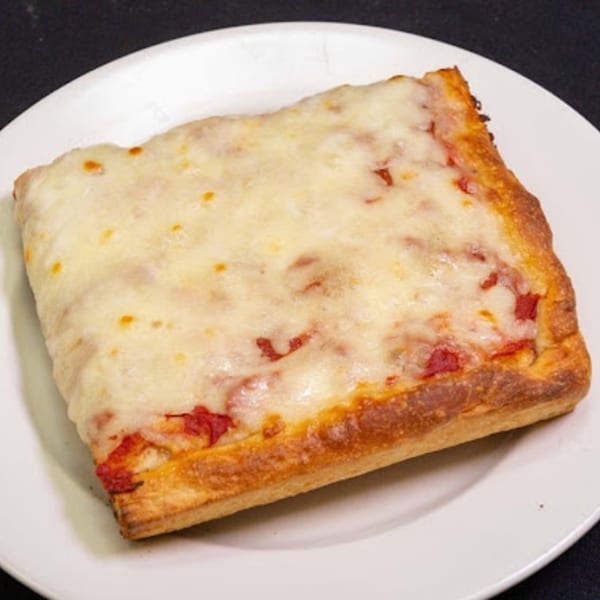 A square slice of Familia Pizza's cheesy Sicilian pizza with a thick crust on a white plate.