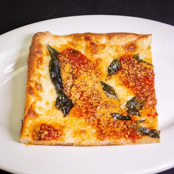 A square slice of Familia Pizza's Italian pizza with cheese, tomato sauce, and basil on a white plate.