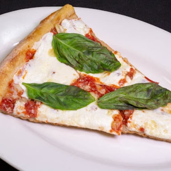 A single slice of Familia Pizza's Margherita pizza with fresh basil on a white plate.