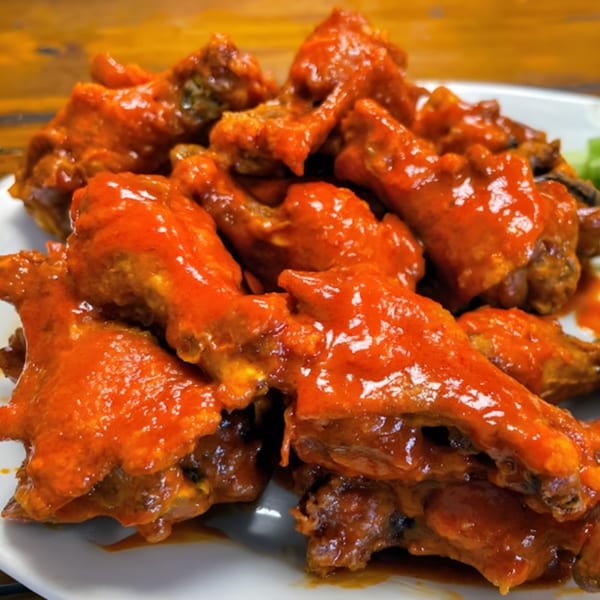 A close-up of a plate piled high with Familia Pizza's buffalo chicken wings, coated in bright orange sauce.