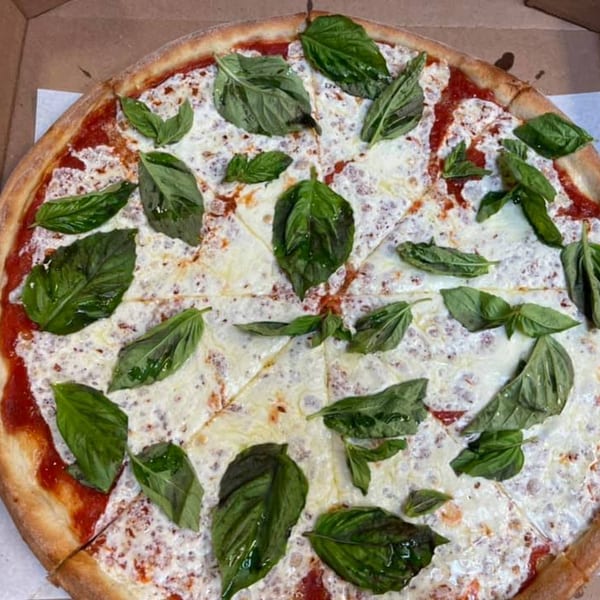 A whole Familia Pizza Margherita, topped with fresh basil leaves, in a cardboard box.